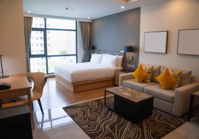 Modern studio apartment design with bedroom and living space. Hotel room panoramic window, king sized bed, couch and coffee table. City flat concept