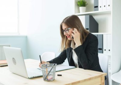 Business, realtor and people concept - Attractive woman in office talking on phone and make notes.